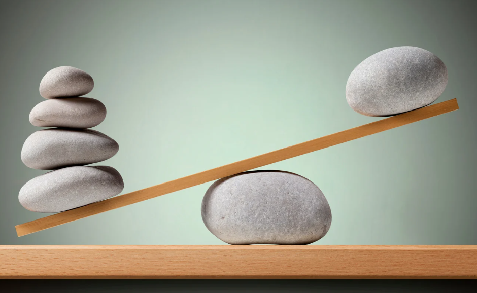 Symbolbild für Zyklusbalance und -beschwerden, Steine balancieren auf Holz
